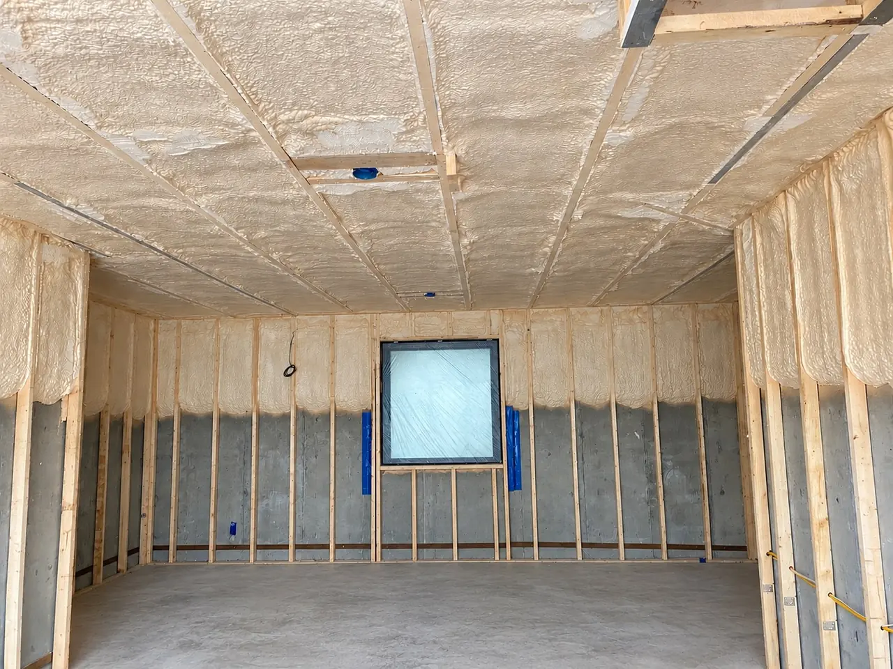Spray foam insulation applied across the ceiling and upper walls of a framed lower-level room.