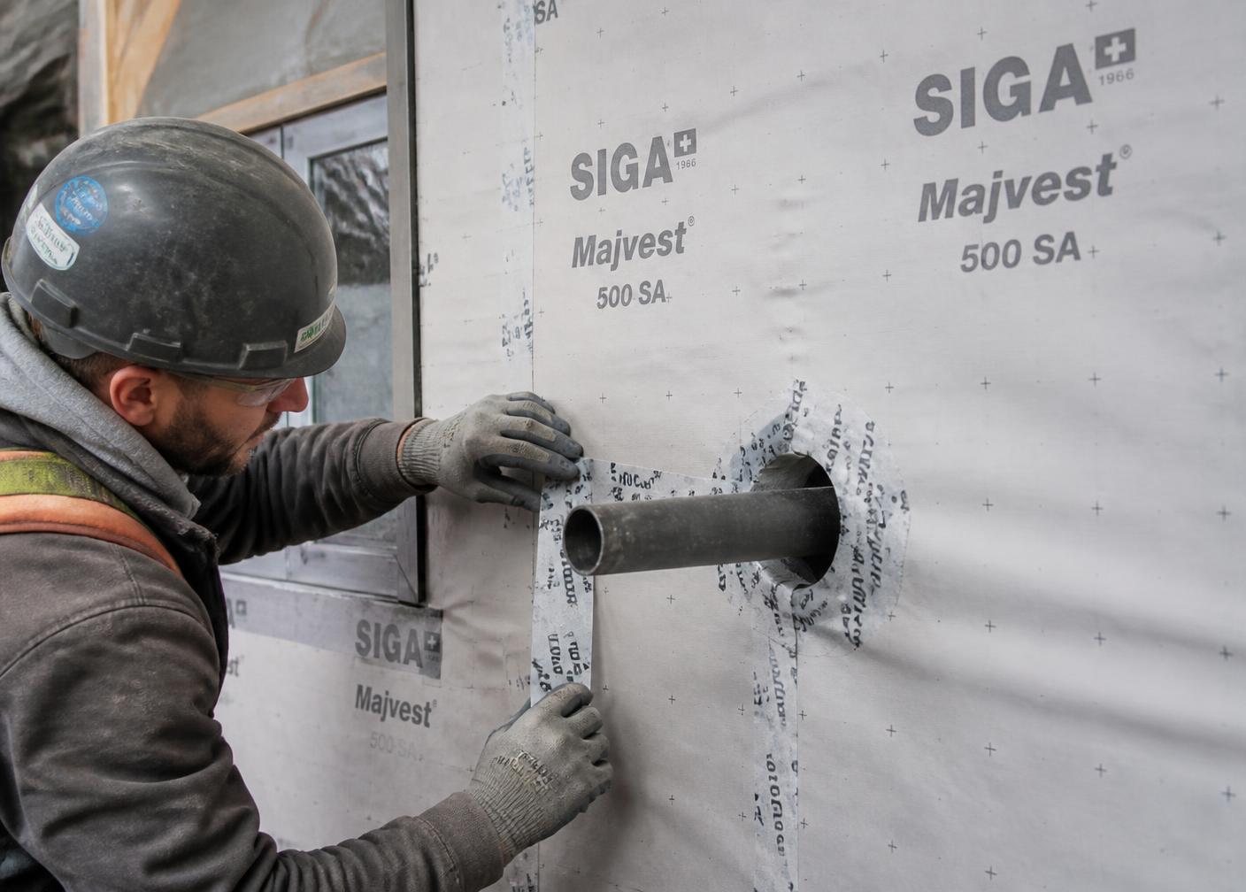 Installer taping an air and vapour barrier membrane around a wall penetration on a job site